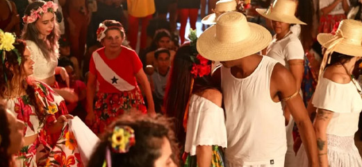 Grupo de pessoas vestidas com trajes típicos participando de uma dança em um evento cultural.