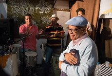 Nei Lopes, referência da cultura afro-brasileira, observando a performance musical enquanto músicos tocam ao fundo.