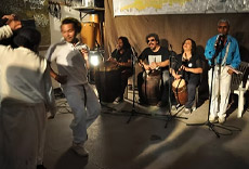 Dançarinos e músicos ao vivo se apresentando em um evento cultural, com destaque para os instrumentos de percussão e os movimentos de dança.
