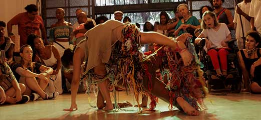 Duas pessoas performando dança contemporânea no centro de uma roda com público atento.