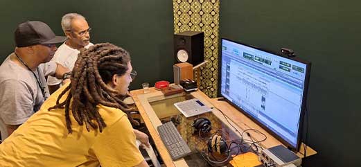 Três pessoas em estúdio de gravação, trabalhando em um projeto de áudio no computador.