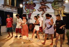 Grupo de pessoas participando de oficina de dança em espaço cultural com pinturas nas paredes.